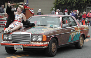 old car decorated with paint, lady in holiday dress sits on hood