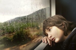 boy sadly looking out window at rain