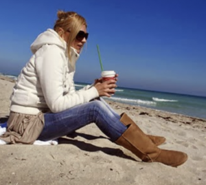 Lady on beach holding coffee dressed warmly