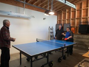 Man of Chinese descent, young man with Down syndrome and his father (Caucasian)play ping pong in the garage