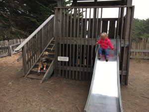 One eyed Jacks slide with little girl in red jacket sliding down as twin brother climbs up the ladder